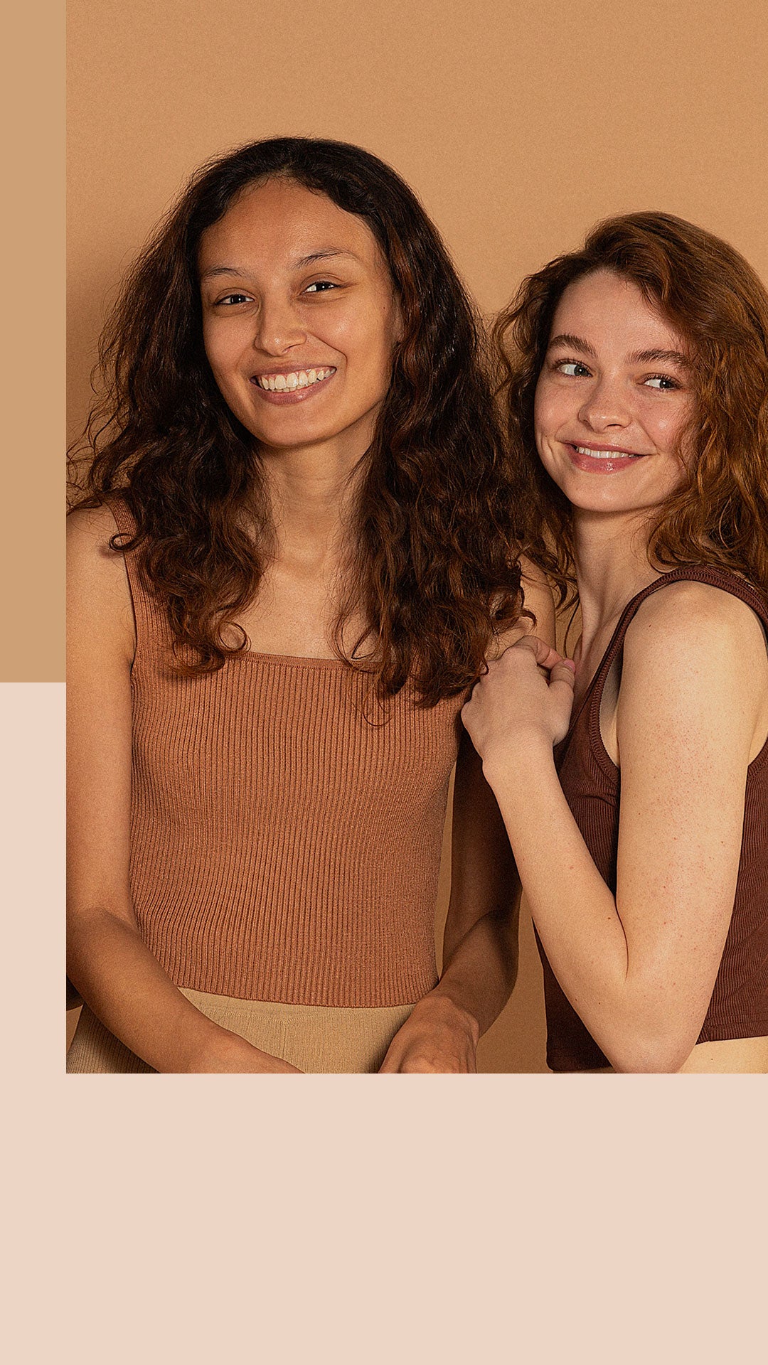 Two young women wearing neutral clothing against a neutral background smiling. 